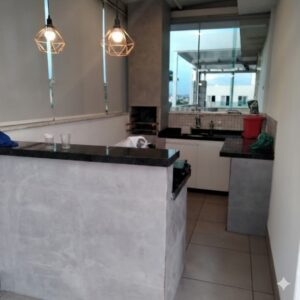 Cozinha americana totalmente reformada com bancada de granito preto em e luminárias com lâmpadas halogênicas.