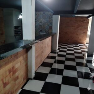 Área gourmet com um piso de porcelanato xadrez, bancada de granito preto assentada sobre uma mureta de tijolinhos à vista.